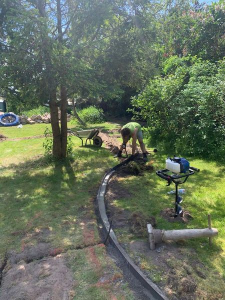 Eine Person gräbt einen Graben neben einem neu verlegten Betonrand in einem grünen Garten.
