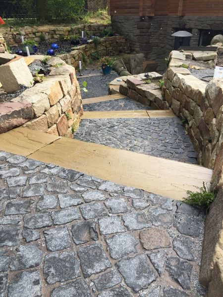 Ein Gartenweg mit steinernen Stufen und Mauern führt abwärts zu einem gepflasterten Bereich.